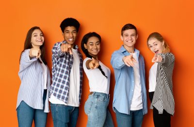 Happy teenagers pointing fingers at camera and smiling Hey, you! Happy teenagers pointing fingers at camera and smiling over orange background